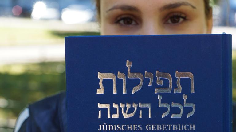 Eine Frau hält ein jüdisches Gebetbuch in die Kamera.