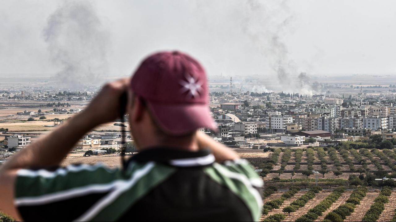 Ein Mann schaut an der türkisch-syrischen Grenze durch ein Fernglas auf die syrische Stadt Ras al-Ain, aus der Rauch aufsteigt Ein Mann schaut an der türkisch-syrischen Grenze durch ein Fernglas auf die syrische Stadt Ras al-Ain, aus der Rauch aufsteigt