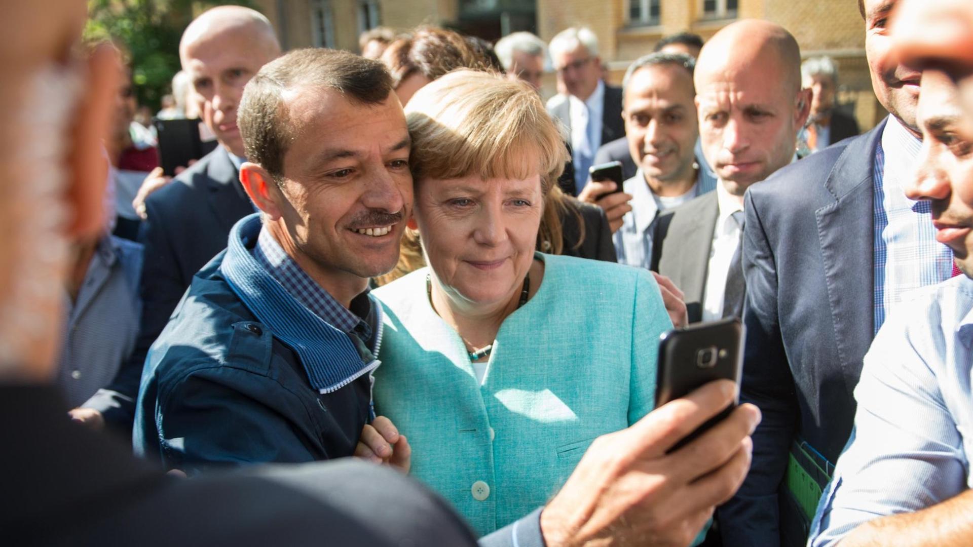 Bundeskanzlerin Angela Merkel (CDU) lässt sich am 10.09.2015 nach dem Besuch einer Erstaufnahmeeinrichtung für Asylbewerber der Arbeiterwohlfahrt (AWO) und der Außenstelle des Bundesamtes für Migration und Flüchtlinge in Berlin-Spandau für ein Selfie zusammen mit einem Flüchtling fotografieren. Foto: Bernd von Jutrczenka/dpa Bundeskanzlerin Angela Merkel (CDU) lässt sich am 10.09.2015 nach dem Besuch einer Erstaufnahmeeinrichtung für Asylbewerber der Arbeiterwohlfahrt (AWO) und der Außenstelle des Bundesamtes für Migration und Flüchtlinge in Berlin-Spandau für ein Selfie zusammen mit einem Flüchtling fotografieren. Foto: Bernd von Jutrczenka/dpa