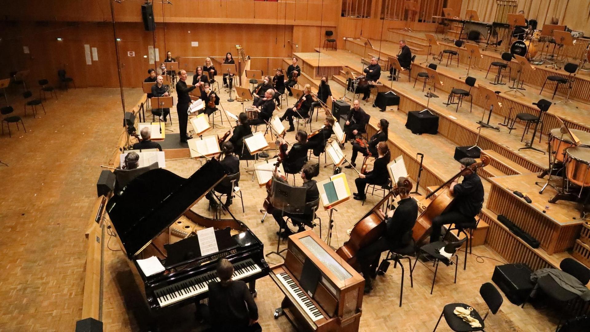 Mitglieder eines Orchesters sitzen breit verteilt in einem Konzertsaal und musizieren vor leeren Rängen. Mitglieder eines Orchesters sitzen breit verteilt in einem Konzertsaal und musizieren vor leeren Rängen.
