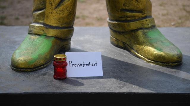28.08.2018, Hessen, Wiesbaden: Ein Schild mit der Aufschrift "Pressefreiheit" und ein Grablicht stehen auf dem Platz der Deutschen Einheit zu Füßen einer goldenen Erdogan-Statue. Die Statue wurde im Rahmen des Kunstfestivals "Wiesbaden Biennale" aufgestellt.