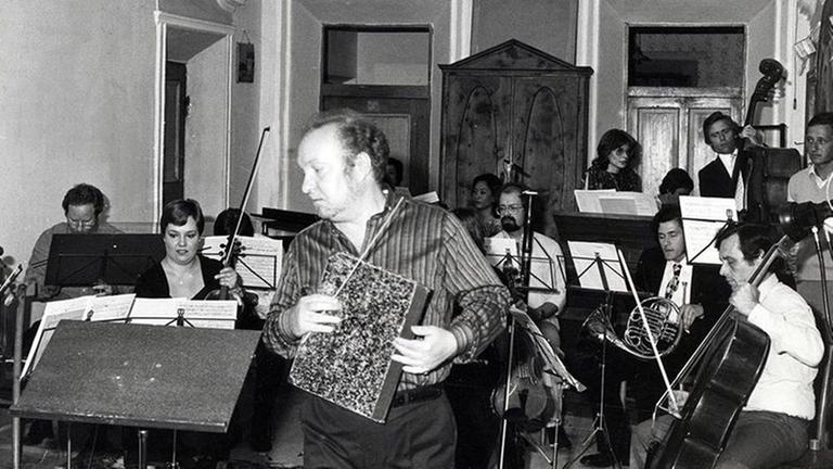 Rainer Riehn mit Noten in der Hand zum Pult gehend, vor dem Ensemble Musica Negativa im Trenkerhof in Toblach Rainer Riehn mit Noten in der Hand zum Pult gehend, vor dem Ensemble Musica Negativa im Trenkerhof in Toblach