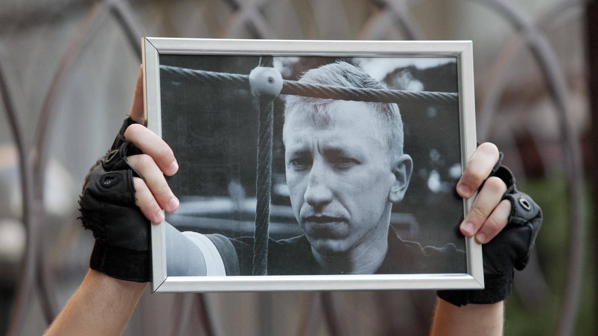 Ein Aktivist in Kiew hält am 3.8.2021 ein Schwarz-Weiß-Porträtfoto des in Kiew tot aufgefundenen belarussischen Aktivisten Vitali Schischow in die Luft. Ein Aktivist in Kiew hält am 3.8.2021 ein Schwarz-Weiß-Porträtfoto des in Kiew tot aufgefundenen belarussischen Aktivisten Vitali Schischow in die Luft.