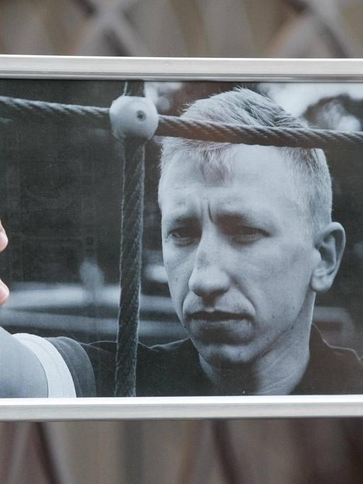 Ein Aktivist in Kiew hält am 3.8.2021 ein Schwarz-Weiß-Porträtfoto des in Kiew tot aufgefundenen belarussischen Aktivisten Vitali Schischow in die Luft.