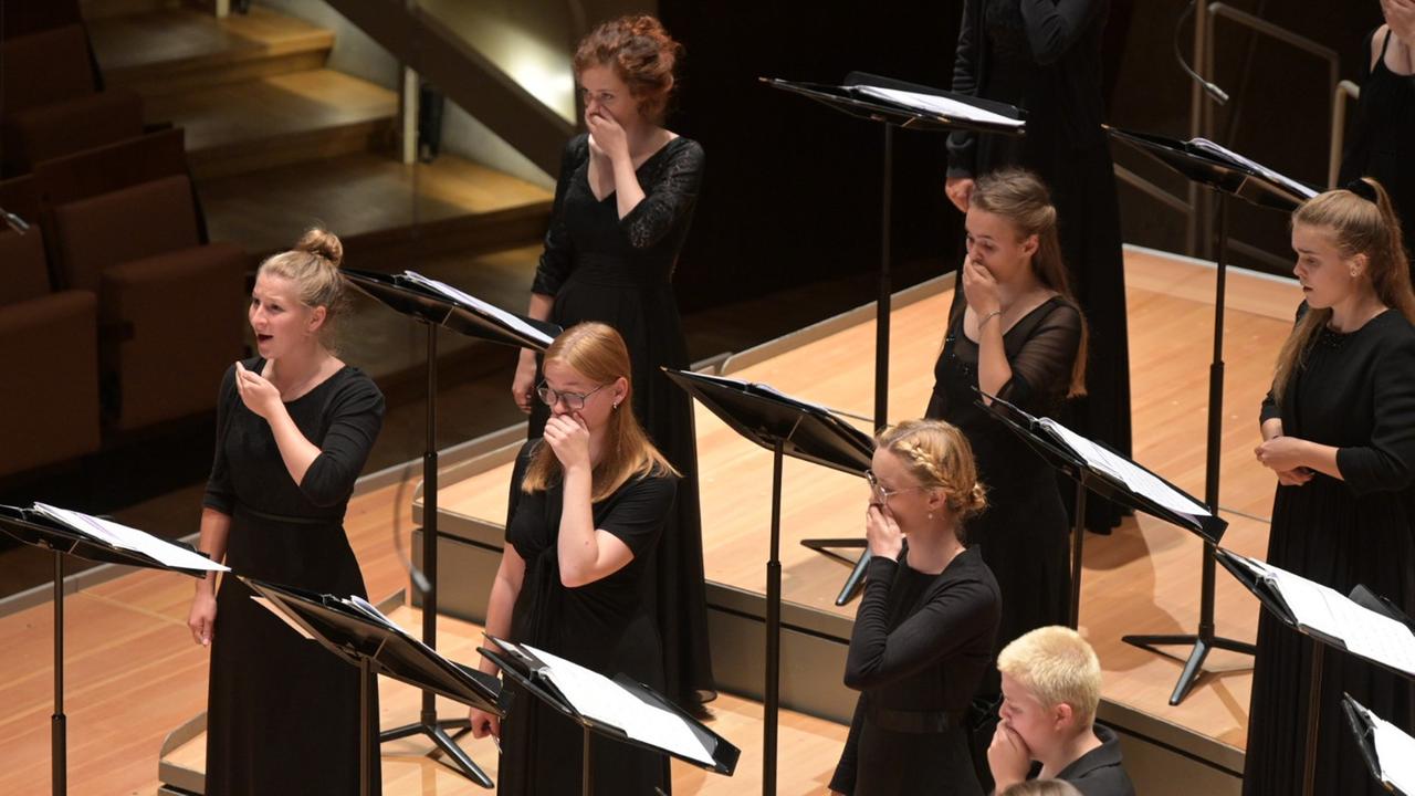 Junge Frauen des Bundesjugendchores halten sich die Hände vor dem Mund beim Singen. Junge Frauen des Bundesjugendchores halten sich die Hände vor dem Mund beim Singen.