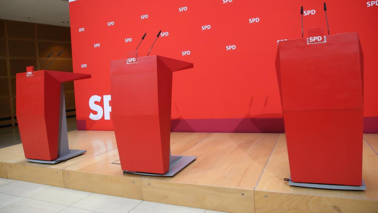 Drei Rednerpulte stehen in der Parteizentrale vor einem roten Hintergrund. Drei Rednerpulte stehen in der Parteizentrale vor einem roten Hintergrund.