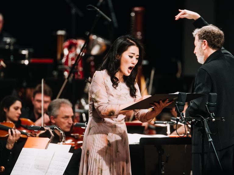 Die Sängerin steht vor dem Orchester neben dem Dirigenten in der Akademie der Künste Berlin.