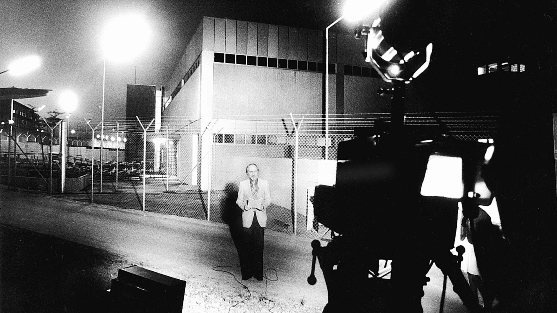 Berichterstattung zum Beginn des RAF-Prozesses vor JVA Stuttgart-Stammheim Mai 1975. Ein Mann steht vor dem Gefängnis, hält ein Blatt Papier in der Hand und spricht in eine Fernsehkamera.