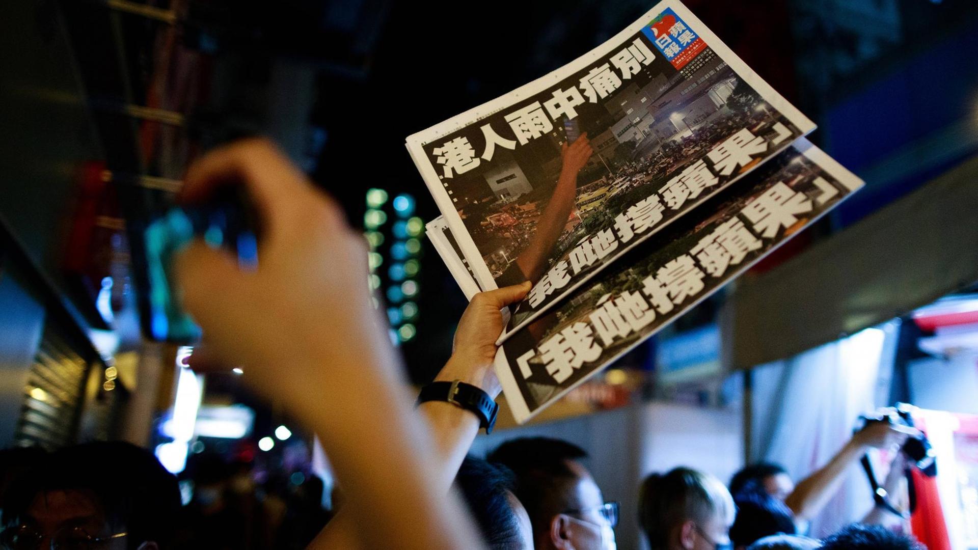 Ein Mann hält zwei exemplare der letzten Ausgabe der Hongkonger Tageszeitung "Apple Daily" in die Höhe.