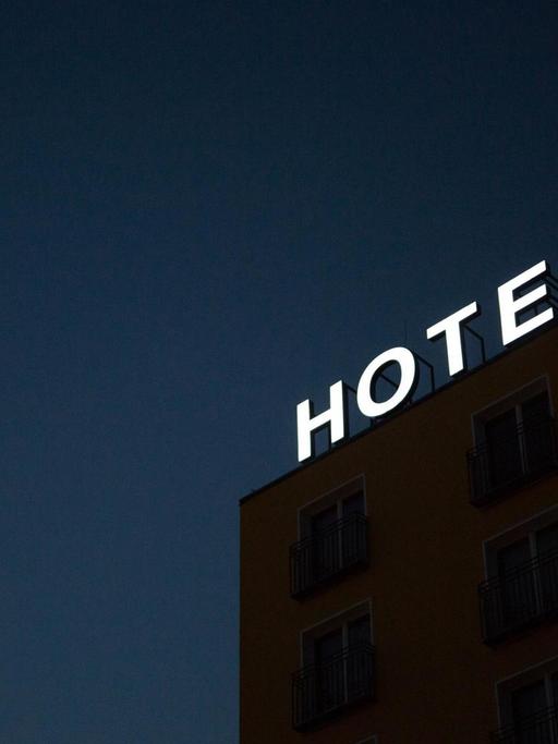 Auf dem Dach eines Gebäudes leuchtet der Schriftzug "HOTEL" vor dem Nachthimmel.