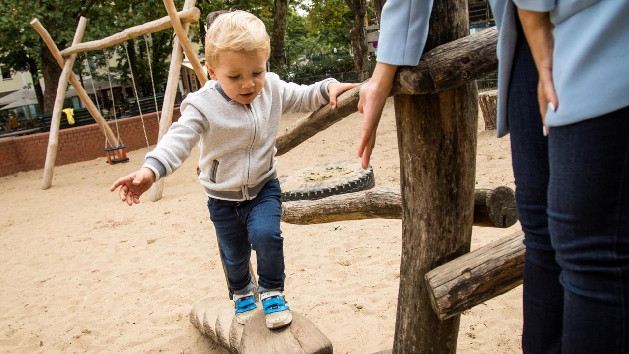 Ein kleiner Junge balanciert auf einem Klettergerüst am Spielplatz.