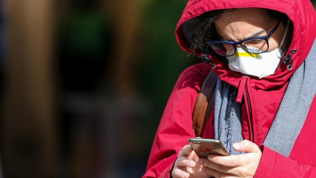 Ein Mann in London mit einer Schutzmaske am 11. März 2020 blickt auf sein Smartphone. Ein Mann in London mit einer Schutzmaske am 11. März 2020 blickt auf sein Smartphone.