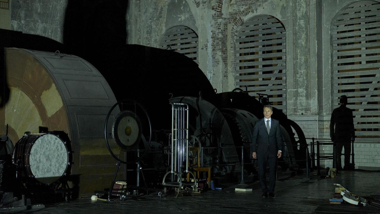 Aufnahme von der Inszenierung: Ein Mann steht vor einer riesigen Turbine.