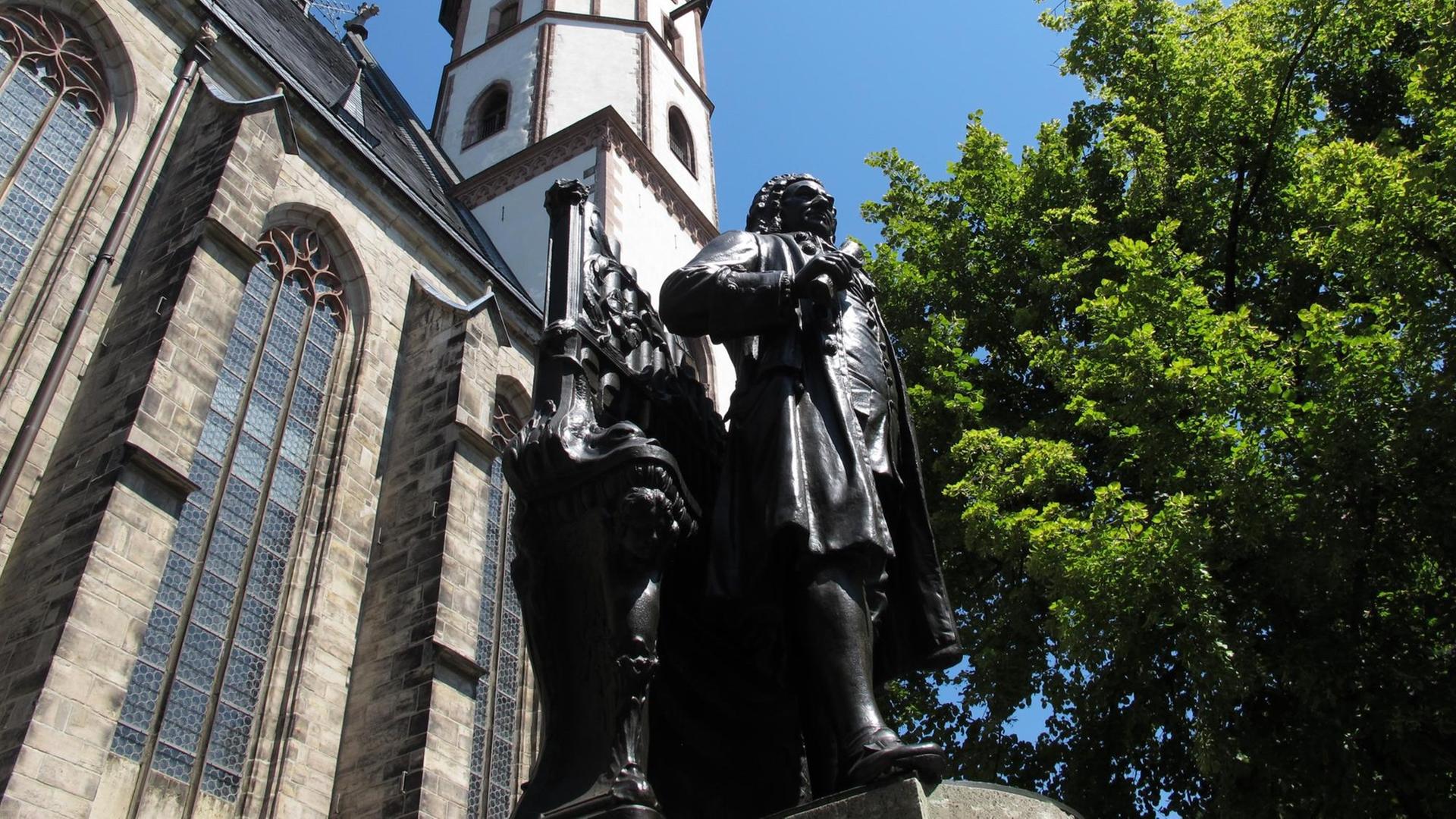 Aus der Froschperspektive fotografiert: das Denkmal von Johann Sebastian Bach. Im Hintergrund die Thomaskirche und ein großer Baum mit grünen Blättern. Aus der Froschperspektive fotografiert: das Denkmal von Johann Sebastian Bach. Im Hintergrund die Thomaskirche und ein großer Baum mit grünen Blättern.
