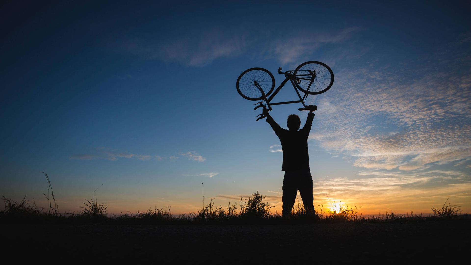 Junger Mann hebt ein leichtes Fahrrad Richtung Himmel Junger Mann hebt ein leichtes Fahrrad Richtung Himmel