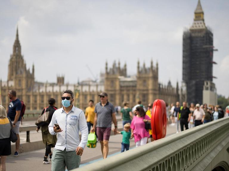 Passanten mit Mund-Nasen-Schutz überqueren die Westminster Bridge in London.