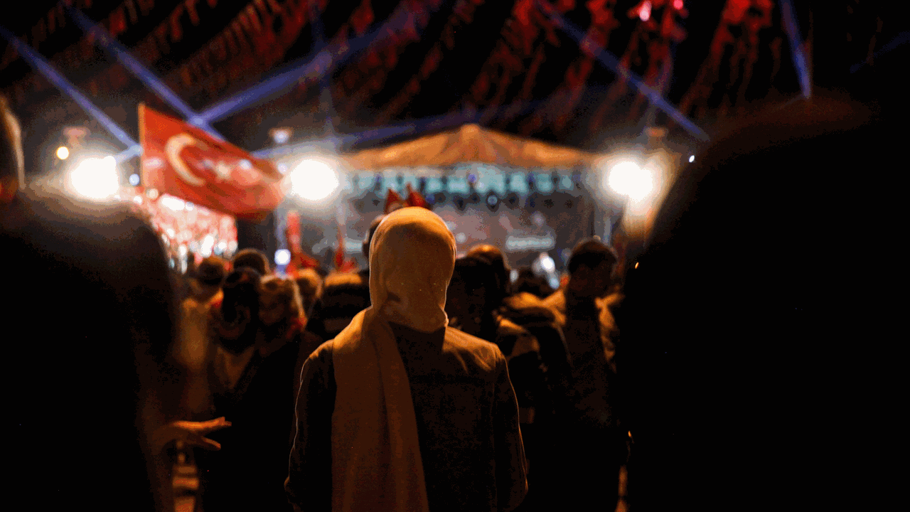 Hazal gerät mitten in den Putschversuch in der Türkei im Jahr 2016. Zu sehen: Demonstration in der Nacht. Eine Frau mit Kopftuch von hinten. Rechts die türkische Fahne. Hazal gerät mitten in den Putschversuch in der Türkei im Jahr 2016. Zu sehen: Demonstration in der Nacht. Eine Frau mit Kopftuch von hinten. Rechts die türkische Fahne.