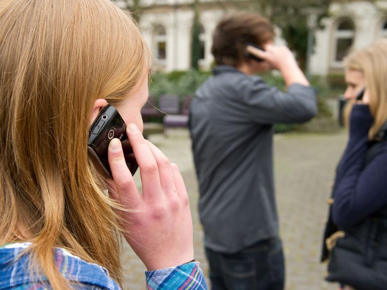 Zehntklässler telefonieren auf einem Schulhof