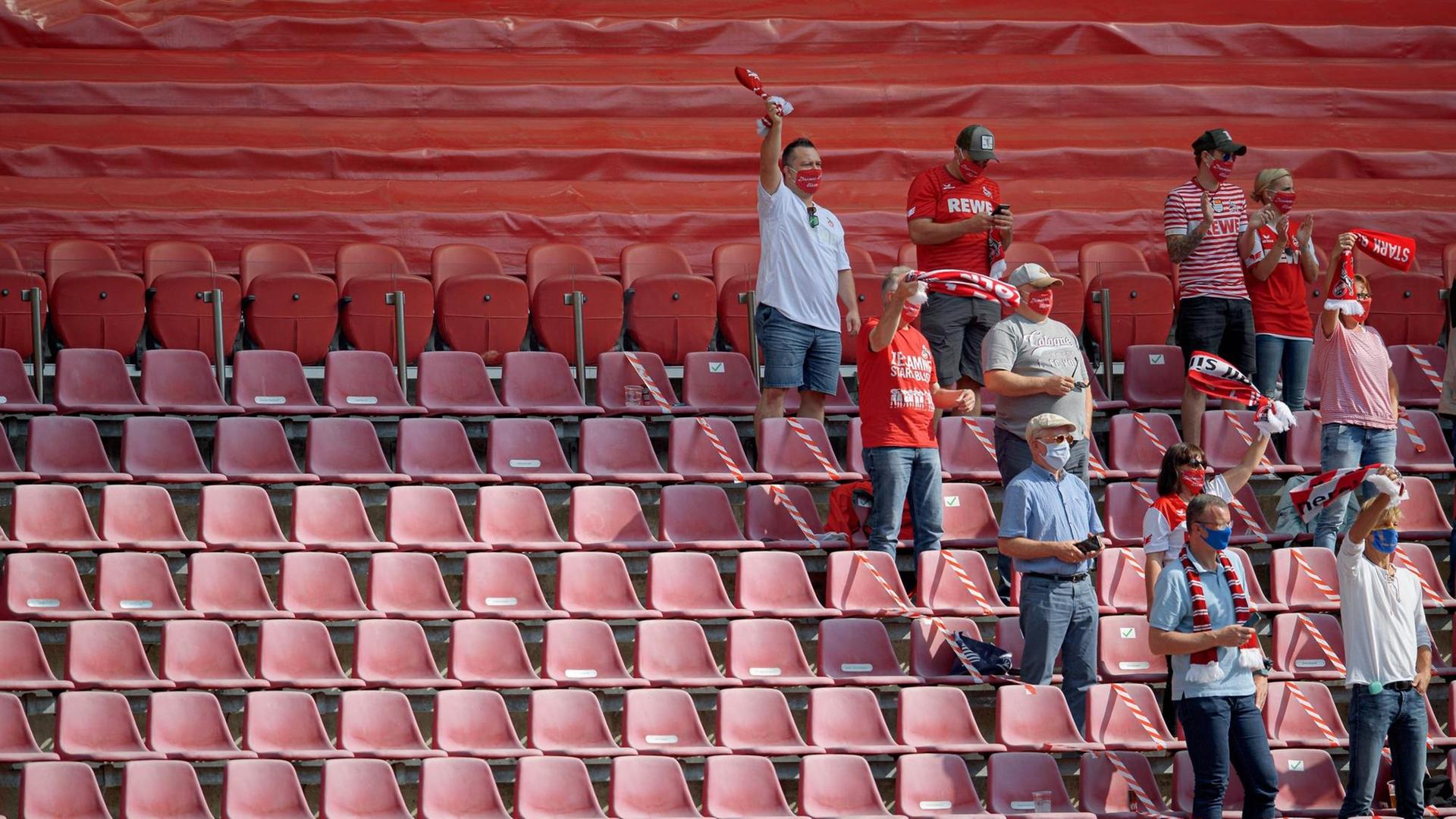 Jubelnde FC Fans mit Mundschutz, auf einer halb leeren Zuschauertribüne in Köln.