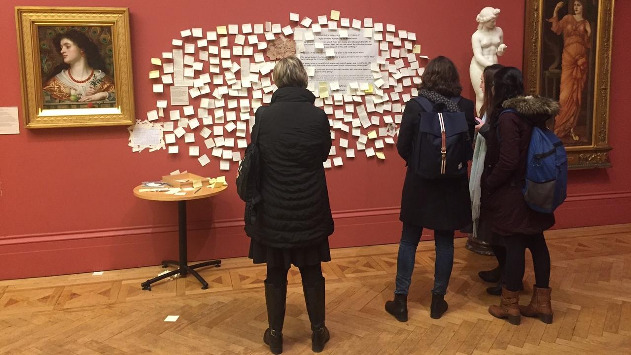 Museums-Besucher stehen vor einer Wand, die mit Klebezetteln bedeckt ist und lesen die Kommentare darauf. Sie hängen dort, wo vorher das Bild "Hylas und die Nymphen" hing, das von der Galerie abgehängt wurde. Museums-Besucher stehen vor einer Wand, die mit Klebezetteln bedeckt ist und lesen die Kommentare darauf. Sie hängen dort, wo vorher das Bild "Hylas und die Nymphen" hing, das von der Galerie abgehängt wurde.