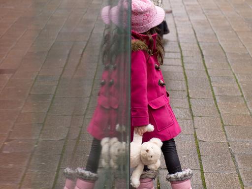 Beschreibung:Ein Mädchen steht am 21.01.2014 in Heilbronn (Baden-Württemberg) mit einem Teddybär an einer Haltestelle und spiegelt sich in einer Scheibe.