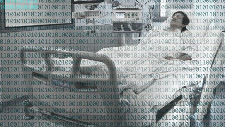 Ein Patient liegt an verschiedene medizinische Geräte angeschlossen in einem Krankenhausbett. Über das gesamte Bild sind binäre Codes gelegt. Ein Patient liegt an verschiedene medizinische Geräte angeschlossen in einem Krankenhausbett. Über das gesamte Bild sind binäre Codes gelegt.