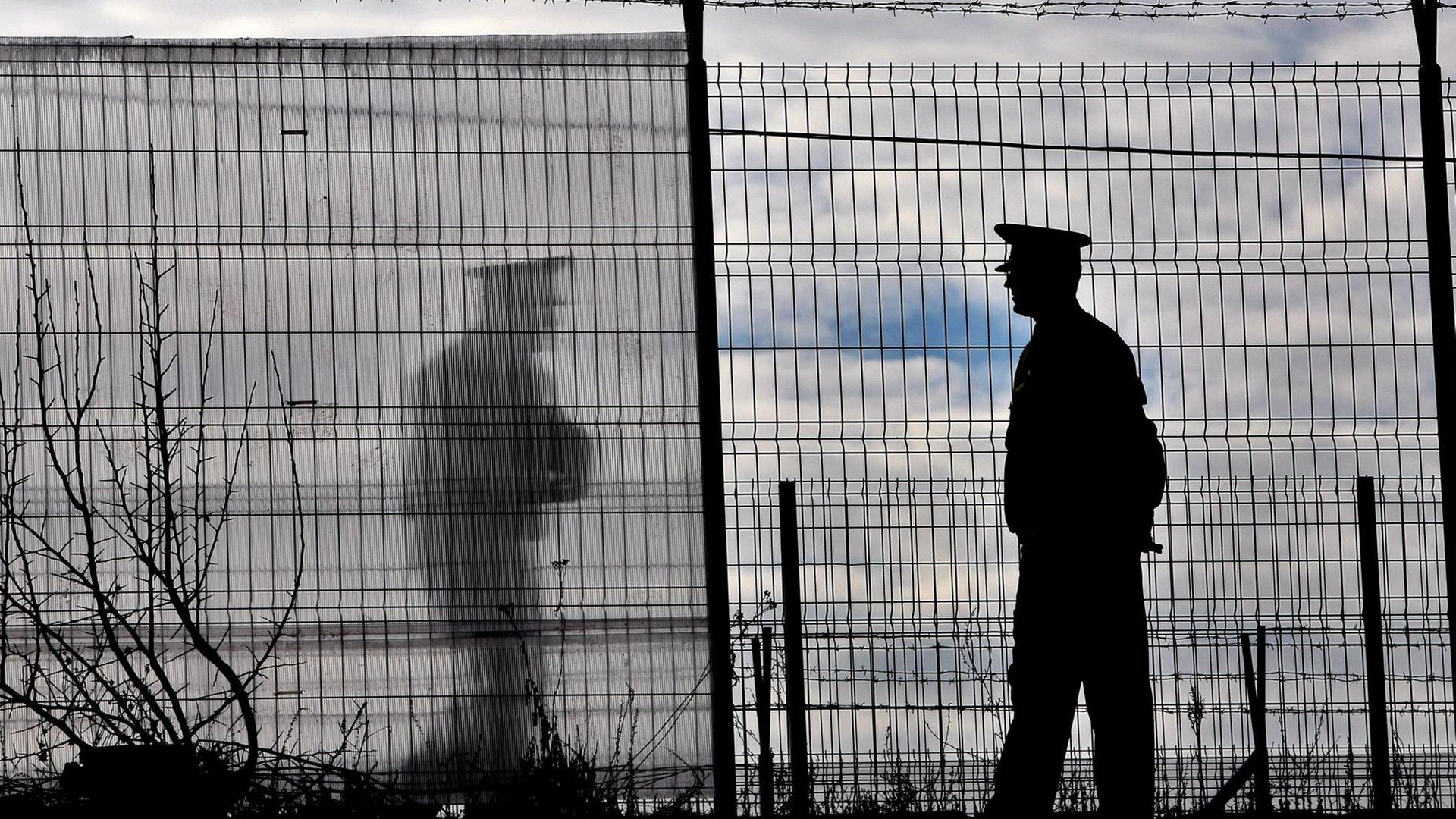 Ein Polizist an einem Grenzzaun. Ein Polizist an einem Grenzzaun.