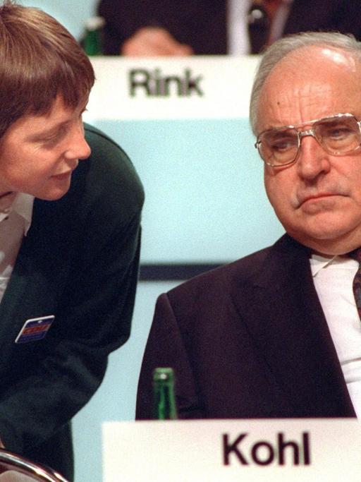 Bundesfrauenministerin Angela Merkel beugt sich am 16.12.1991 während des CDU-Parteitags in Dresden zu ihrem Mentor, Bundeskanzler Kohl, herab. Die Diplom-Physikerin, heute Generalsekretärin der Christdemokraten, wird auf dem CDU-Parteitag vom 9. bis 11.4.2000 in Essen für den Parteivorsitz kandidieren. Die 45-Jährige wäre die erste Frau an der Spitze der Unionspartei - eine Blitzkarriere: Während der Wende engagierte sie sich im "Demokratischen Aufbruch". Nach den ersten freien Volkskammerwahlen war sie stellvertretende Regierungssprecherin der DDR und trat im August 1990 in die Union ein. 1991 holte Kanzler Kohl sie als Ministerin für Frauen und Jugend in sein Kabinett, 1993 wurde sie CDU-Landesvorsitzende in Mecklenburg- Vorpommern, 1994 Bundesumweltministerin. Nach der Niederlage der Christdemokraten bei den Bundestagswahlen 1998 wurde sie zur Generalsekretärin ihrer Partei gewählt.