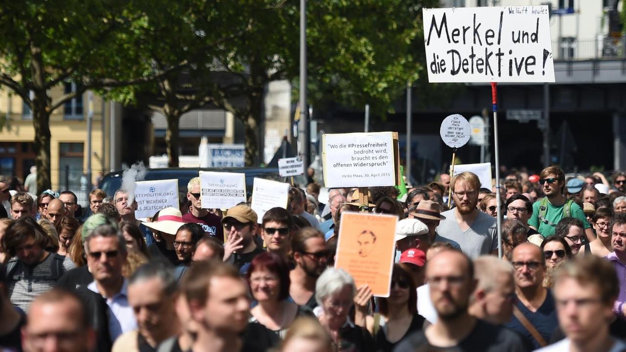 Teilnehmer einer Demonstration von Unterstützern von Netzpolitik.org halten ein Schild hoch, auf dem "Merkel und die Detektive!" steht
