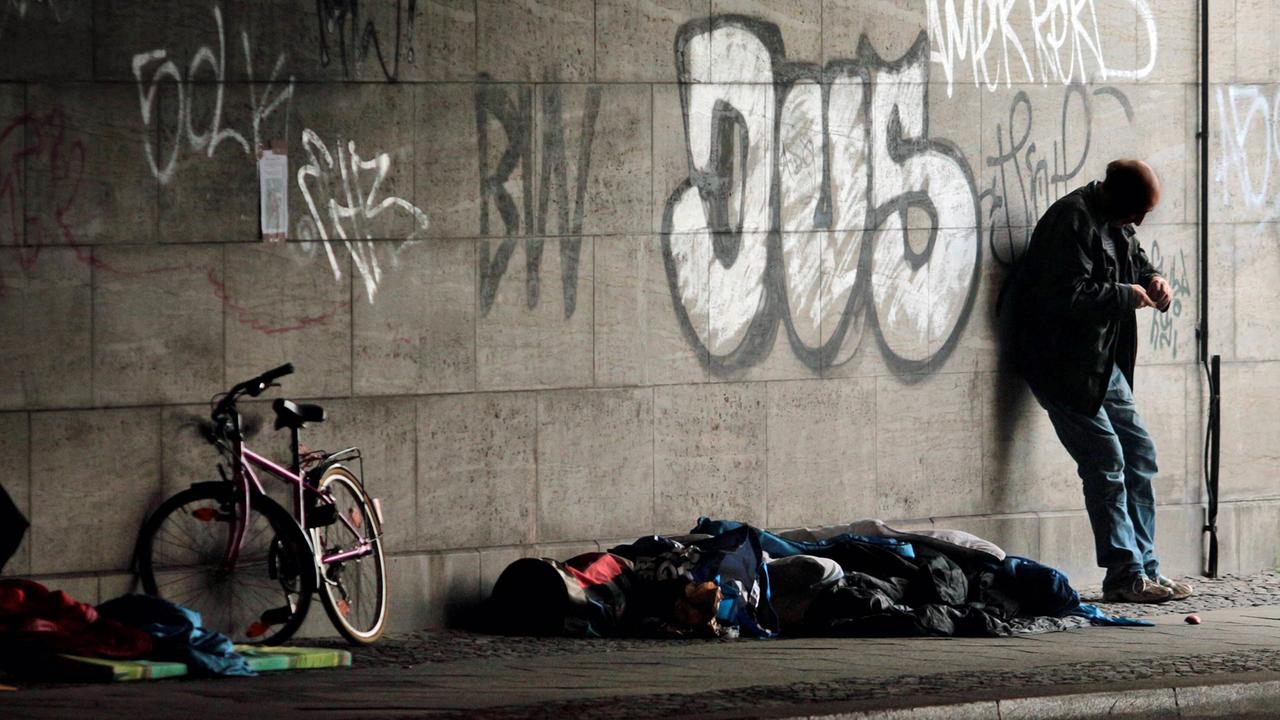 Ein obdachloser Mann steht am 9.8.2016 neben einem Schlafsack und einem Fahrrad unter einer Brücke am Bahnhof Zoo in Berlin. Ein obdachloser Mann steht am 9.8.2016 neben einem Schlafsack und einem Fahrrad unter einer Brücke am Bahnhof Zoo in Berlin.