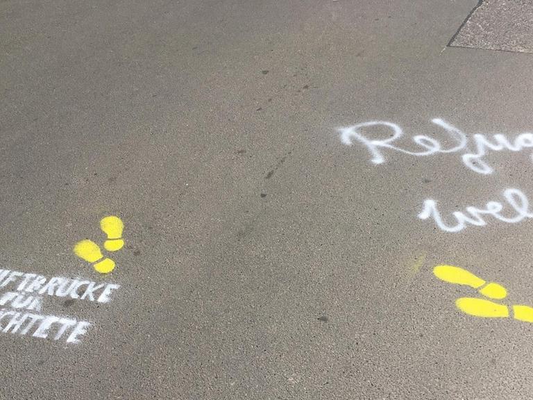 Auf den Asphalt sind gelbe Fußstapfen gemalt und mit weißer Schrift: "Luftbrücke für Geflüchtete" und "Refugees welcome here".