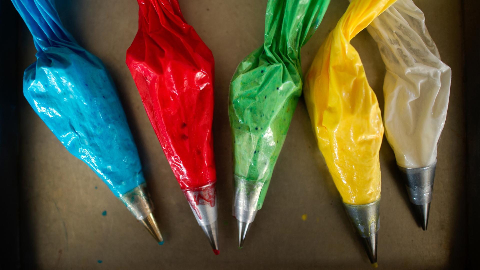 Zuckergusstüten mit Lebensmittelfarbe in verschiedenen Farben liegen auf einem Tisch in einer Bäckerei. Zuckergusstüten mit Lebensmittelfarbe in verschiedenen Farben liegen auf einem Tisch in einer Bäckerei.