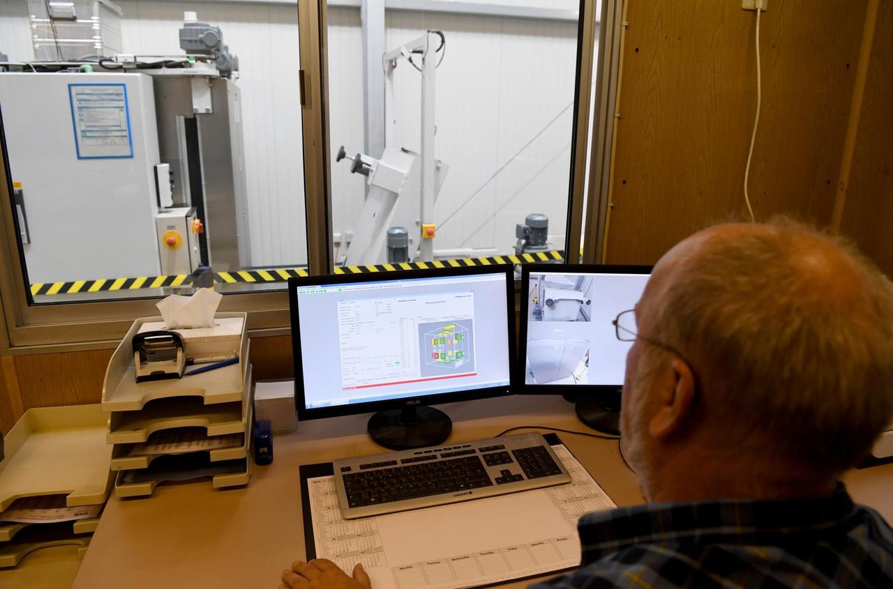 An Mann sitzt vor einem Computer. im Hintergrund sieht man die Maschine, mit der die Radioaktivität des untersuchten Materials ermittelt wird An Mann sitzt vor einem Computer. im Hintergrund sieht man die Maschine, mit der die Radioaktivität des untersuchten Materials ermittelt wird