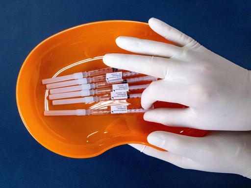 Zwei Hände in Handschuhen halten die ettiketierten Impfdosen 