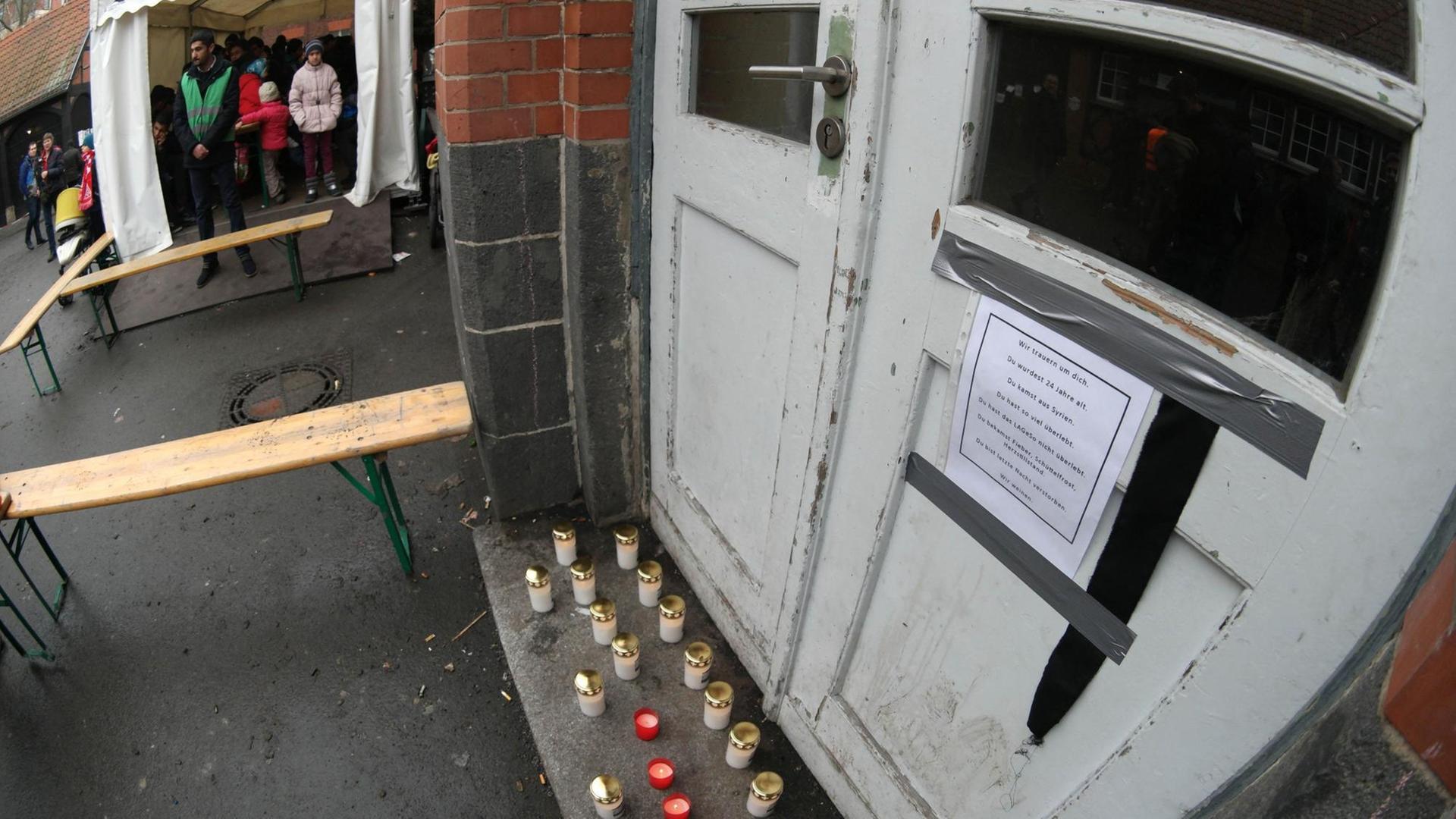 Vor einer Außentür stehen weiße und rote Kerzen, an der Tür hängt eine Trauerbotschaft.