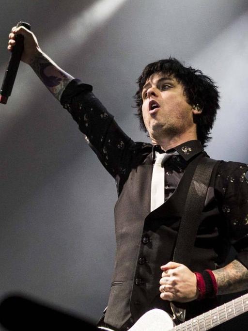Billie Joe Armstrong von der US-Punkband Green Day steht auf einer Konzertbühne und reckt eine Faust hoch.