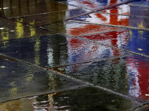 Flaggen spiegeln sich auf dem regennassen Pflaster vor dem britischen Parlament