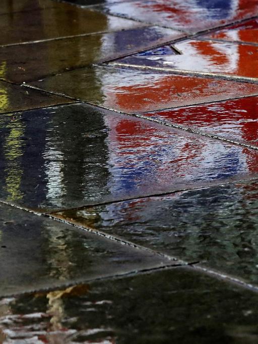 Flaggen spiegeln sich auf dem regennassen Pflaster vor dem britischen Parlament