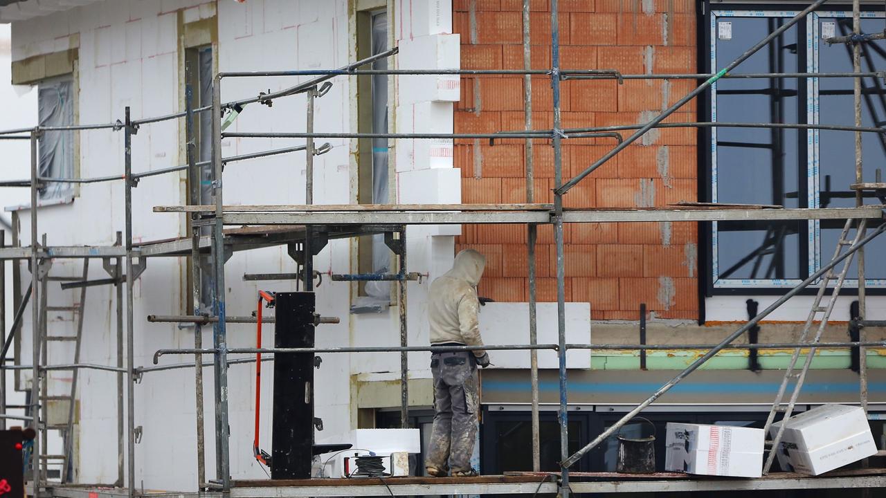 Ein Handwerker bringt auf einem Baugrundstück Dämmmaterial an. Ein Handwerker bringt auf einem Baugrundstück Dämmmaterial an.