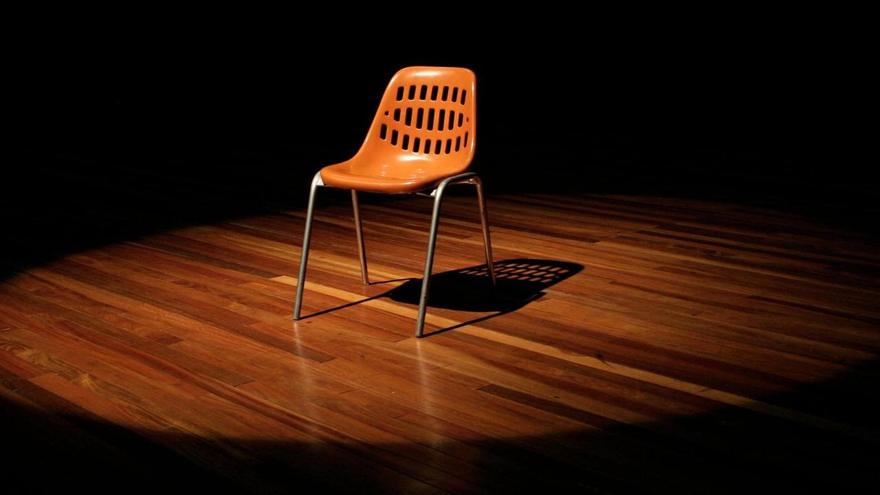 Ein leerer Stuhl steht auf einer Theaterbühne.