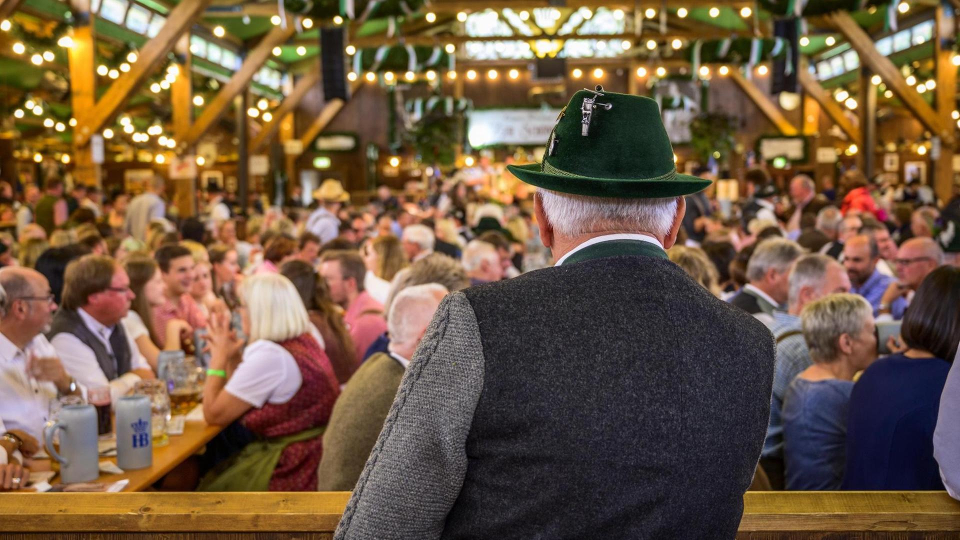 Ein Mann in Tracht blickt in die Weite eines Festzelts auf dem Oktoberfest. Ein Mann in Tracht blickt in die Weite eines Festzelts auf dem Oktoberfest.