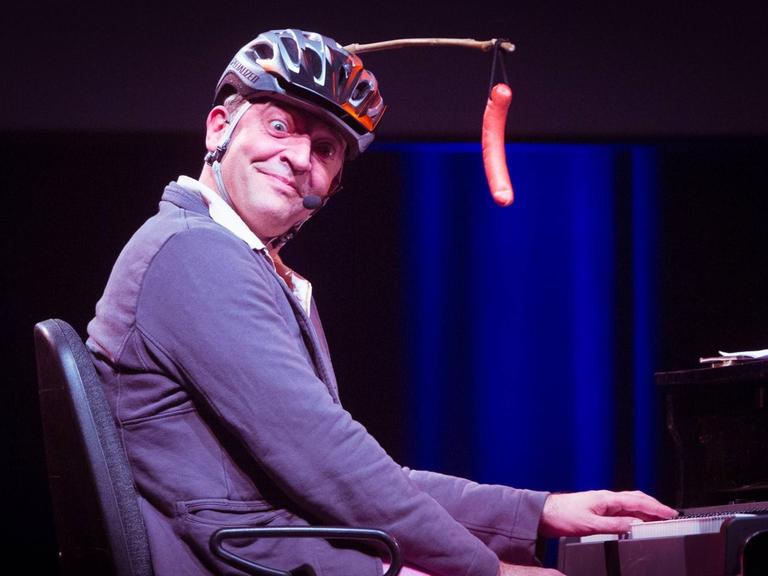 Reinald Grebe mit guter Laune beim Sächsischen Unternehmerpreis im Alten Schlachthof. Auf dem Kopf trägt er einen Fahrradhelm und ein Wiener Würstchen an einer Stange.
