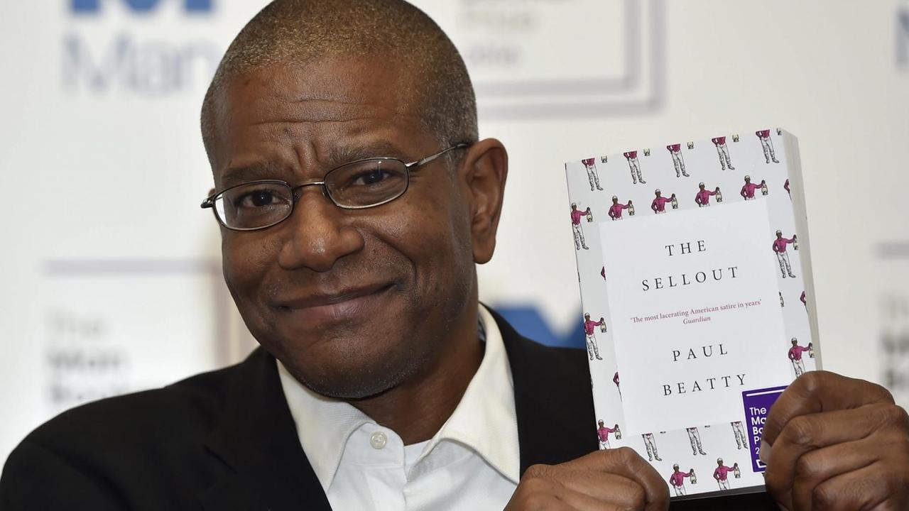 Der Afro-Amerikaner Beatty hält das Buch lächelnd neben seinen Kopf. Im Hintergrund eine Wand, auf der man unscharf die Logos des "Man Booker Prize" sieht.