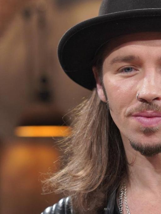 Gil Ofarim mit langen Haaren, schwarzem Hut und schwarzer Lederjacke.