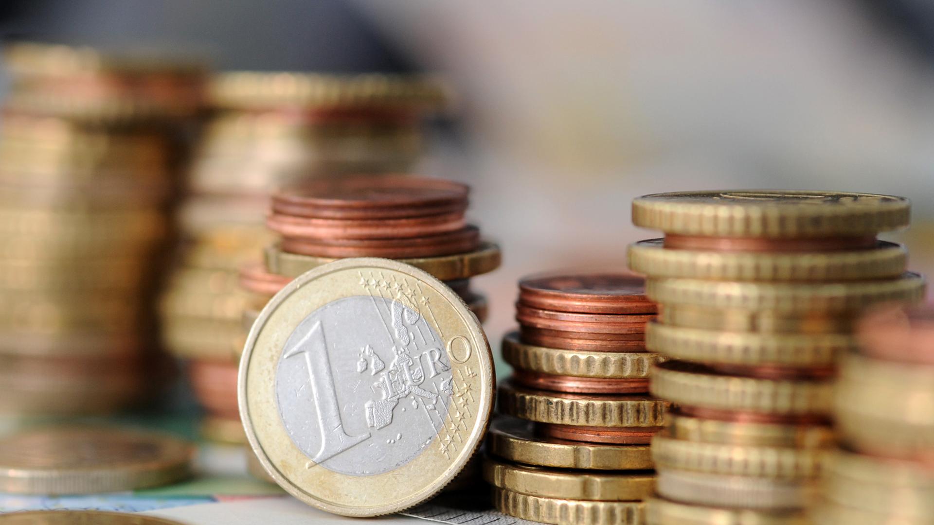 Eine Ein-Euro-Münze und einige Stapel von verschiedenen anderen Münzen Eine Ein-Euro-Münze und einige Stapel von verschiedenen anderen Münzen