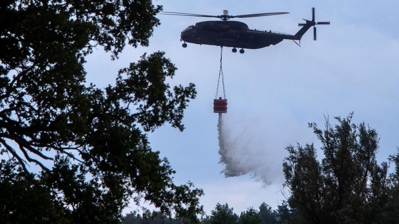 03.07.2019, Mecklenburg-Vorpommern, Jessenitz: Ein Hubschrauber der Bundeswehr wirft Löschwasser über dem brennenden Waldgebiet ab. Die Lage im Waldbrandgebiet auf einem ehemaligen Truppenübungsplatz bei Lübtheen in Mecklenburg-Vorpommern hat sich erstmals seit Ausbruch des Feuers leicht entspannt. Erste Bewohner konnten in ihre vorsorglich geräumten Häuser zurückkehren. Foto: Jens Büttner/dpa-Zentralbild/dpa | Verwendung weltweit 03.07.2019, Mecklenburg-Vorpommern, Jessenitz: Ein Hubschrauber der Bundeswehr wirft Löschwasser über dem brennenden Waldgebiet ab. Die Lage im Waldbrandgebiet auf einem ehemaligen Truppenübungsplatz bei Lübtheen in Mecklenburg-Vorpommern hat sich erstmals seit Ausbruch des Feuers leicht entspannt. Erste Bewohner konnten in ihre vorsorglich geräumten Häuser zurückkehren. Foto: Jens Büttner/dpa-Zentralbild/dpa | Verwendung weltweit