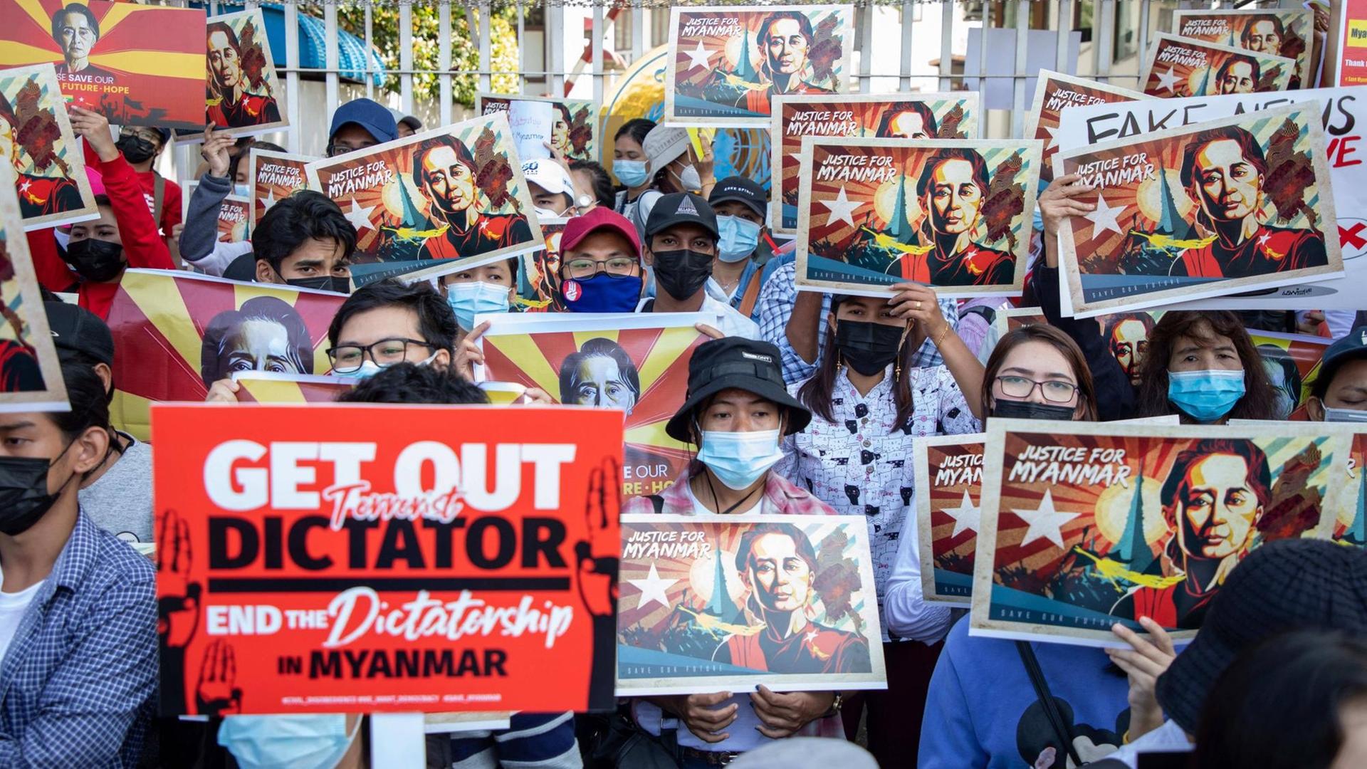 Junge Demonstrierende in Myanmar halten Schilder mit dem Porträt von Aung San Suu Kyi hoch. Ein Demonstrant hält ein rotes Schild mit der Aufschrift "Get out Dictator". Junge Demonstrierende in Myanmar halten Schilder mit dem Porträt von Aung San Suu Kyi hoch. Ein Demonstrant hält ein rotes Schild mit der Aufschrift "Get out Dictator".