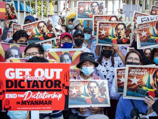 Junge Demonstrierende in Myanmar halten Schilder mit dem Porträt von Aung San Suu Kyi hoch. Ein Demonstrant hält ein rotes Schild mit der Aufschrift "Get out Dictator".