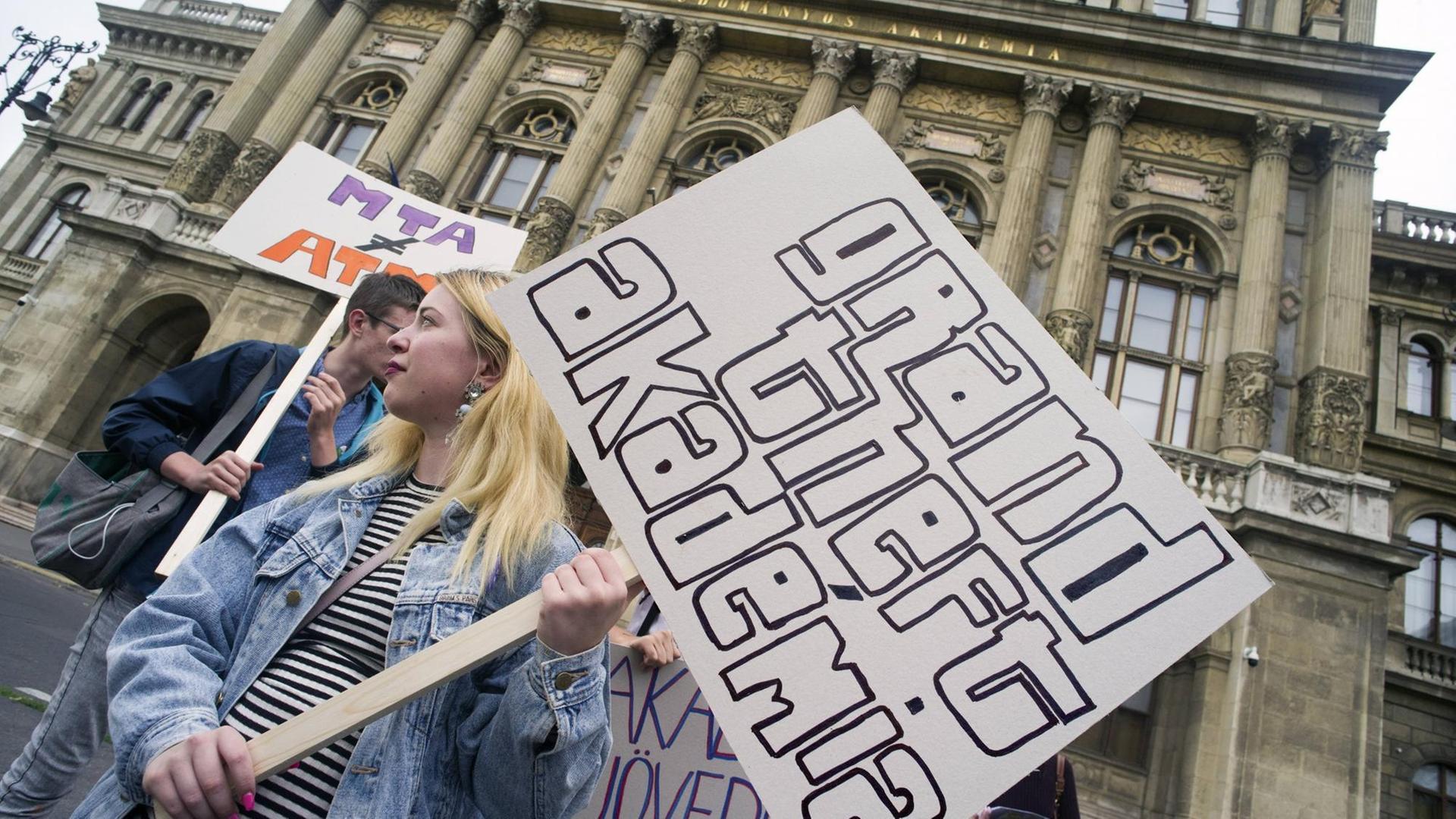 Eine Demonstrantin vor der Akademie der Wissenschaften in Budapest hält ein Schild mit der Aufschrift "Grand Theft Akadémia" Eine Demonstrantin vor der Akademie der Wissenschaften in Budapest hält ein Schild mit der Aufschrift "Grand Theft Akadémia"