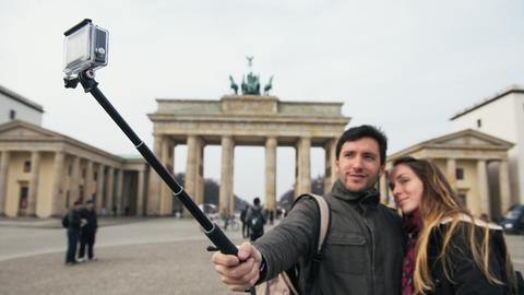 Zwei Touristen machen am Brandenburger Tor in Berlin ein Selbstporträt mit einem "Selfie-Stick"